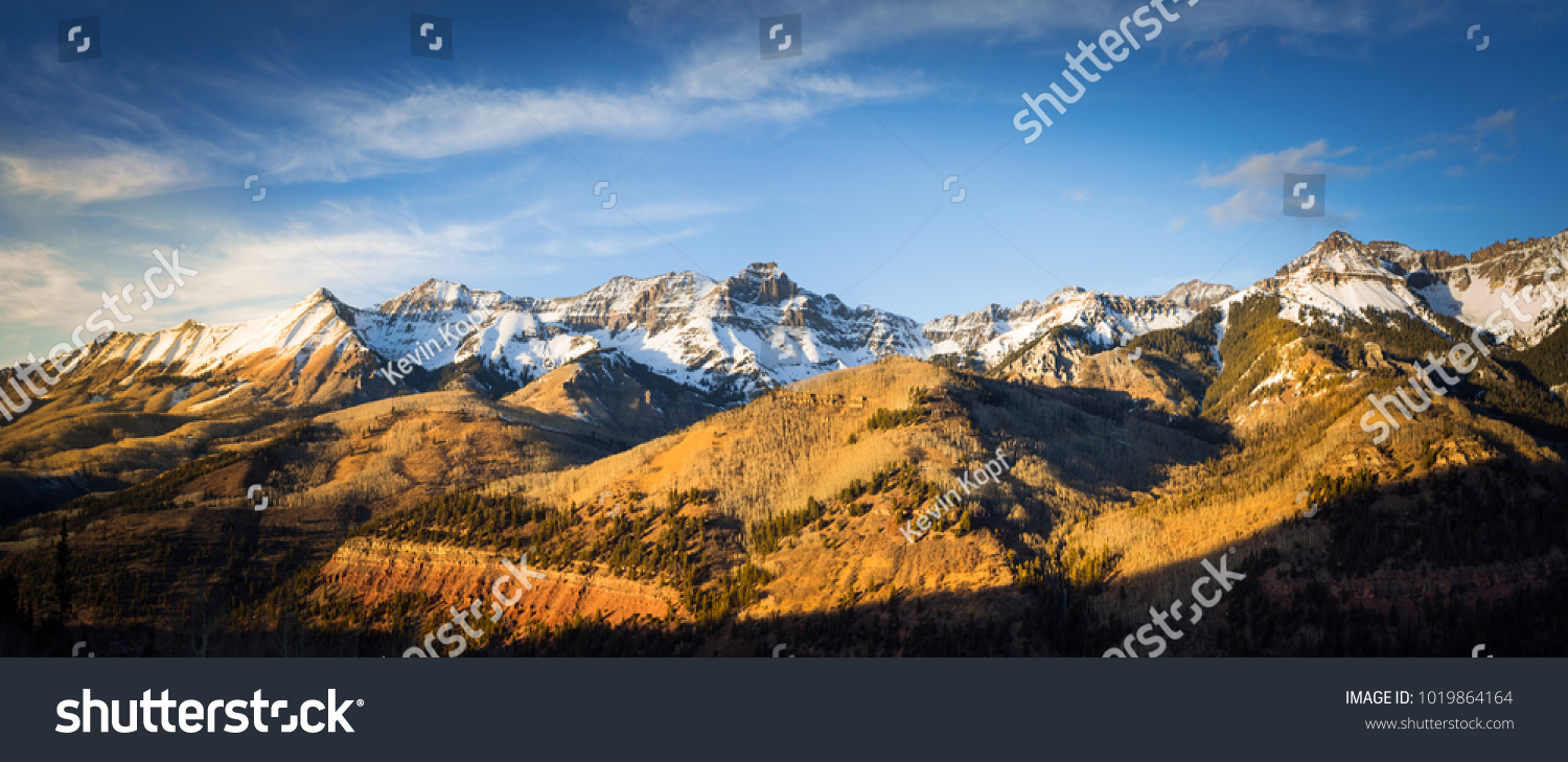 Panoramatický výhled na úbočí hory osvětlené zapadajícím sluncem ve skalnatých horách. Záře slunce osvětluje podzimní barvy, spolu s prvním sněhem nalezeným vysoko v horských vrcholcích. #1019864164