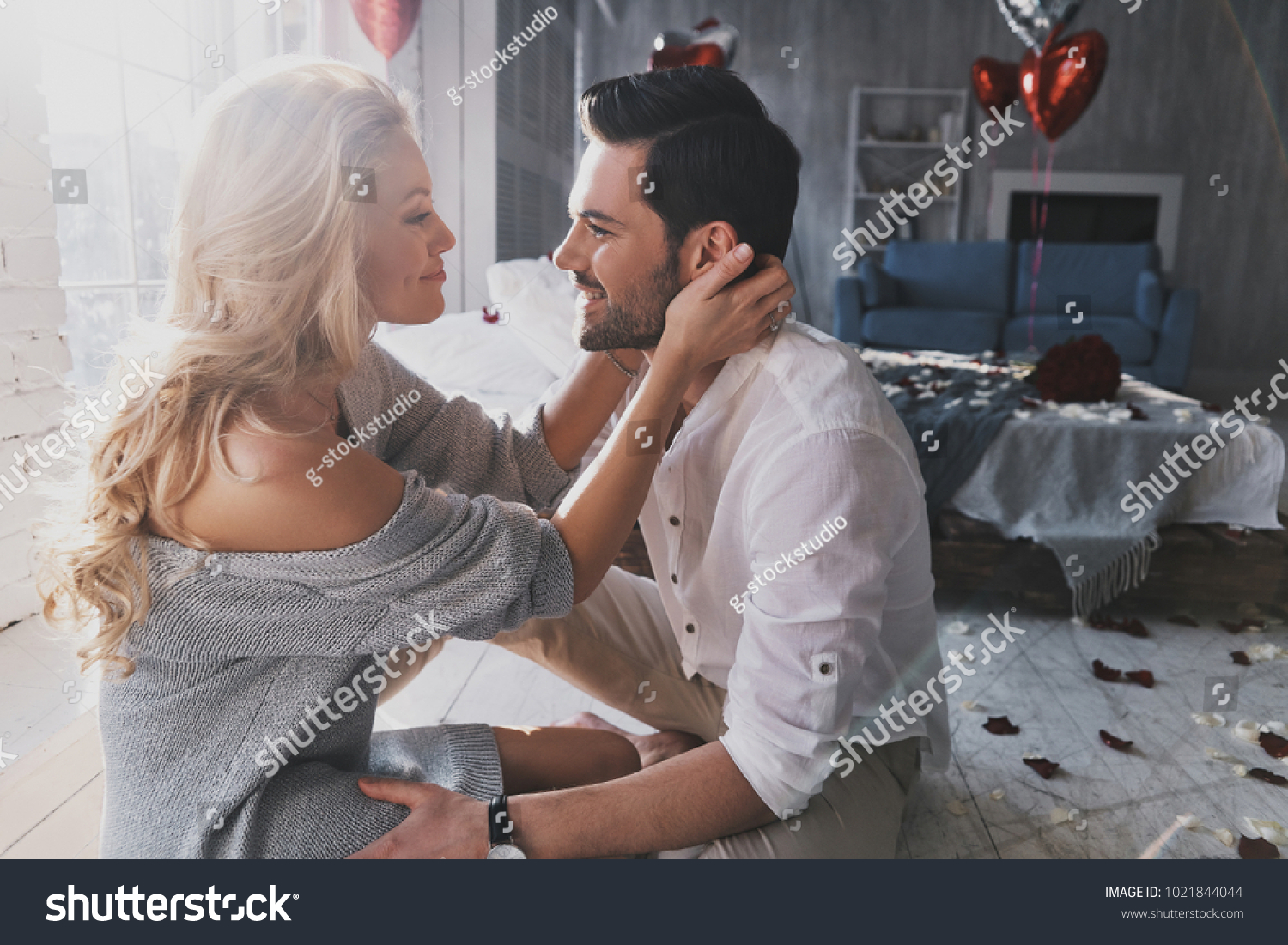 She is the center of his universe. Beautiful young couple looking at each other while sitting in the bedroom #1021844044