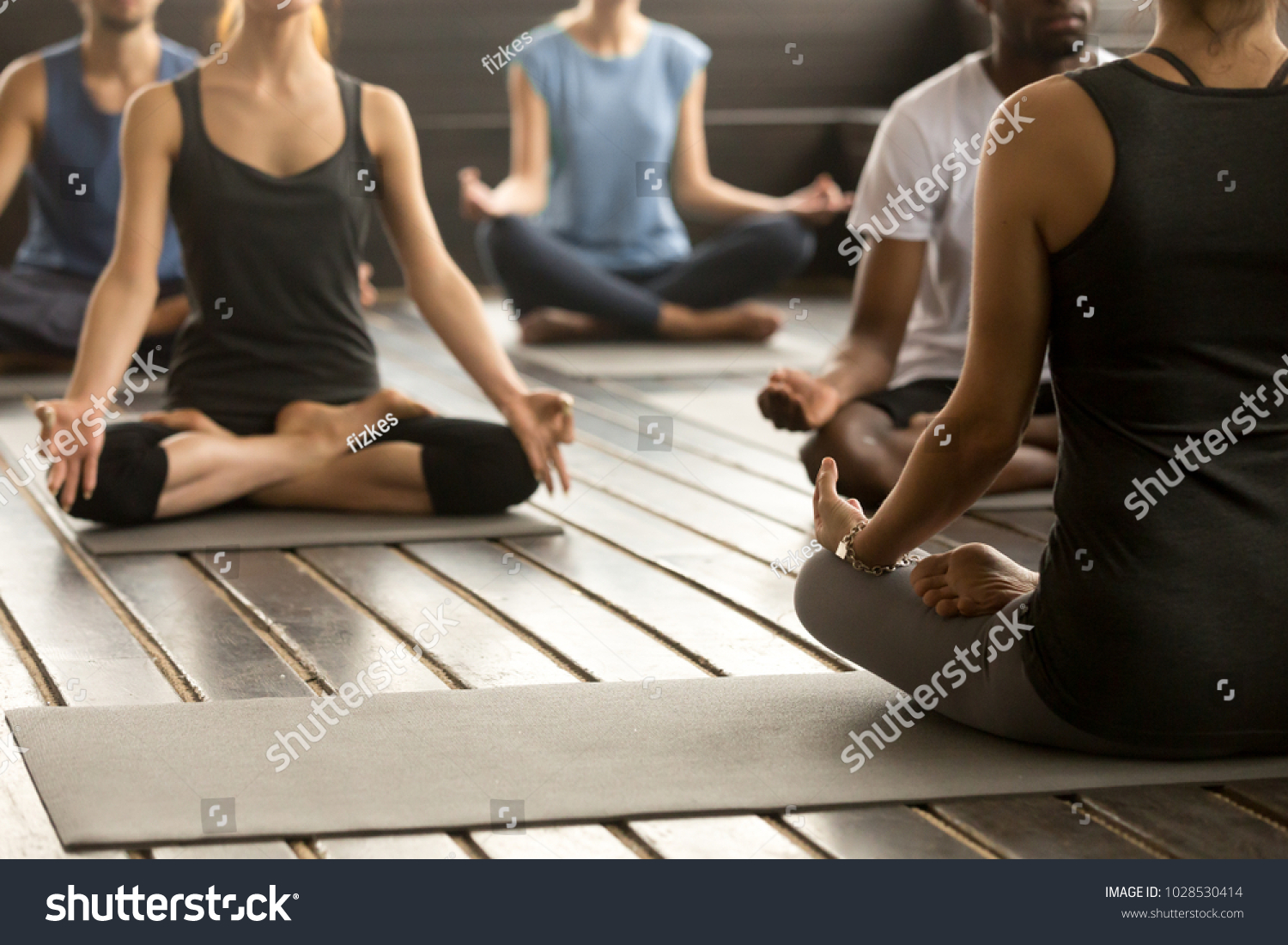 Group of young sporty people practicing yoga lesson with instructor, sitting in Sukhasana exercise, Easy Seat pose, working out, students training in sport club, studio close up, back view #1028530414