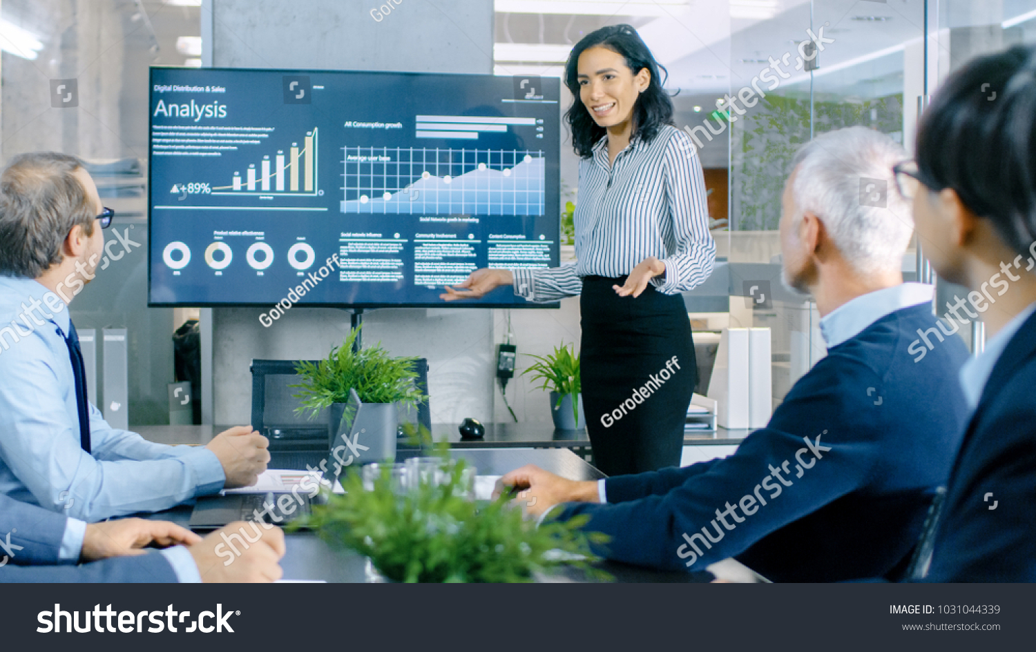 Beautiful Businesswoman Gives Report/ Presentation to Her Business Colleagues in the Conference Room, She Shows Graphics, Pie Charts and Company's Growth on the Wall TV. #1031044339