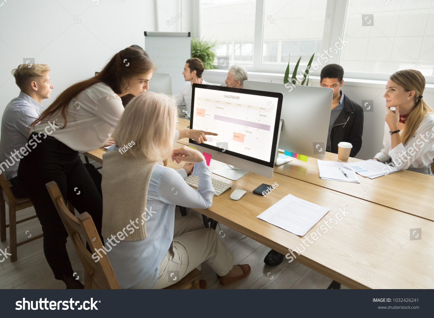 Young manager teaching senior worker explains planning work in office, corporate teacher helps older employee with application, aged woman using calendar on group computer training, mentoring concept #1032426241