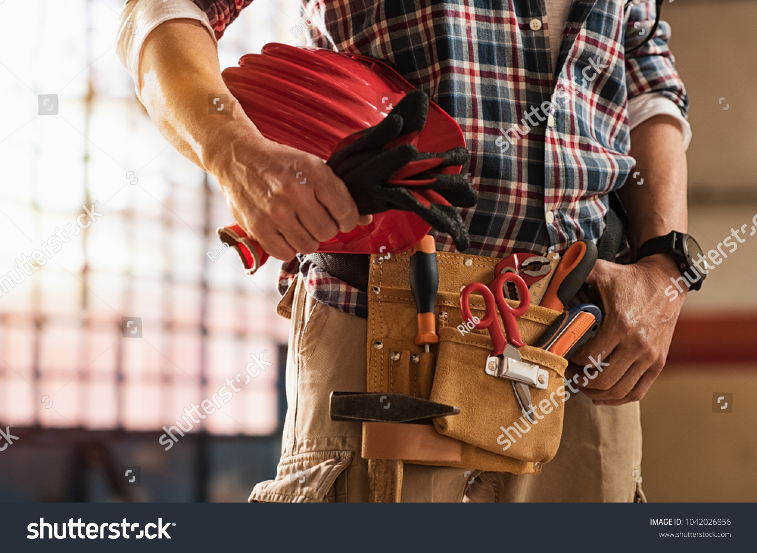 Closeup of bricklayer hands holding hardhat and construction equipment. Detail of mason man hands holding work gloves and wearing tool kit on waist. Handyman with tools belt and artisan equipment. #1042026856