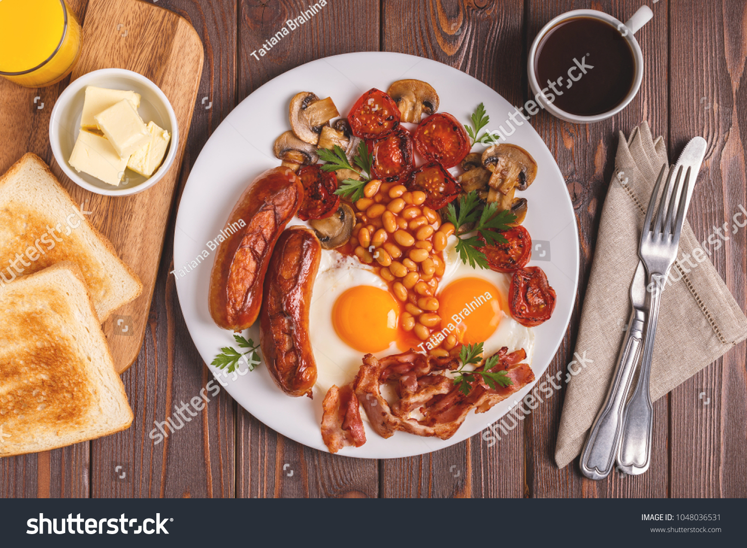 Traditional full English breakfast with fried eggs, sausages, beans, mushrooms, grilled tomatoes and bacon on wooden background. Top view #1048036531