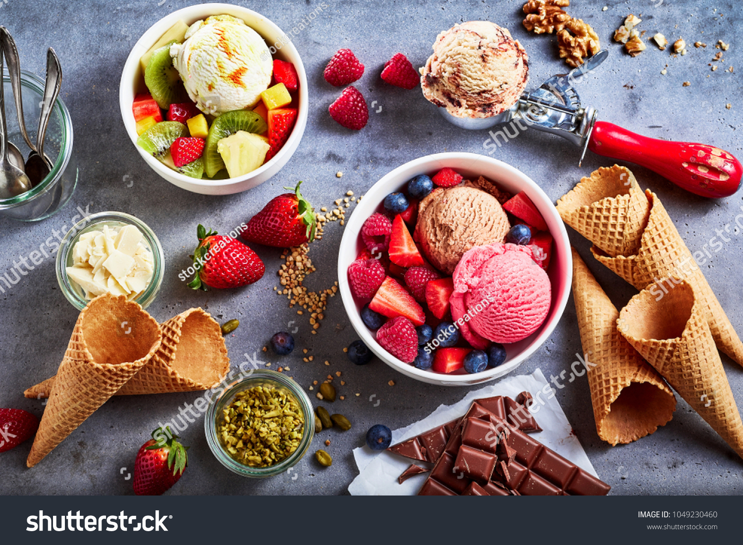 Fresh fruit with scoops of creamy speciality ice cream in assorted flavors with raspberry, berry, blueberry, strawberry, walnut , pistachio, chocolate, sugar cones and a scoop for serving from above #1049230460