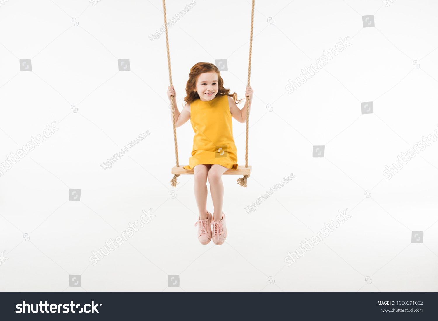 Little stylish child in dress riding on swing isolated on white #1050391052