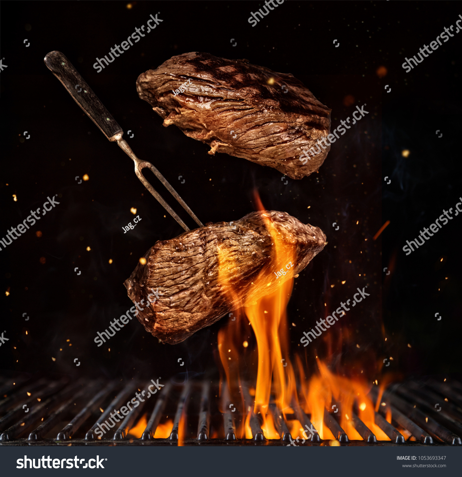 Flying beef steaks over flaming grill grid, isolated on black background. Barbecue and cooking #1053693347