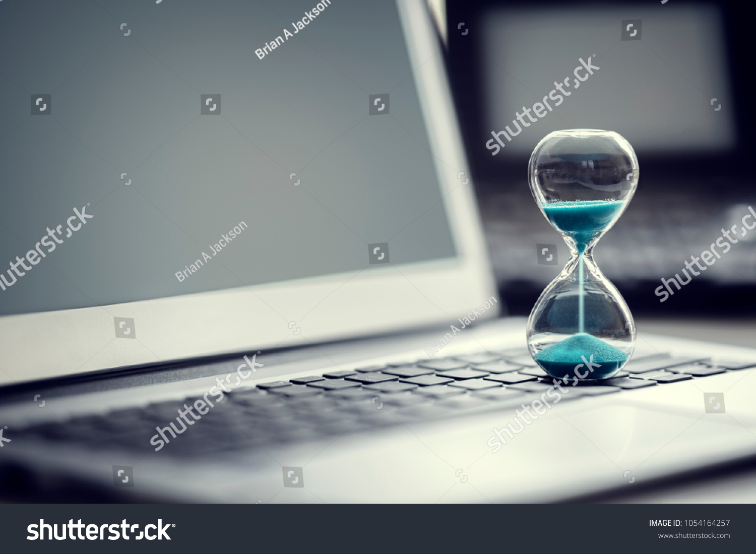 Hourglass on laptop computer concept for time management and countdown to deadline #1054164257