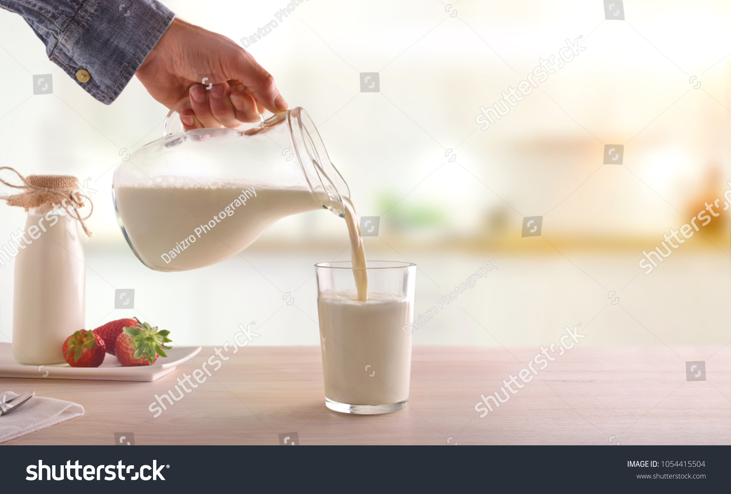 Serving breakfast milk with a jug in a glass on a white wooden kitchen table. Horizontal composition. Front view #1054415504