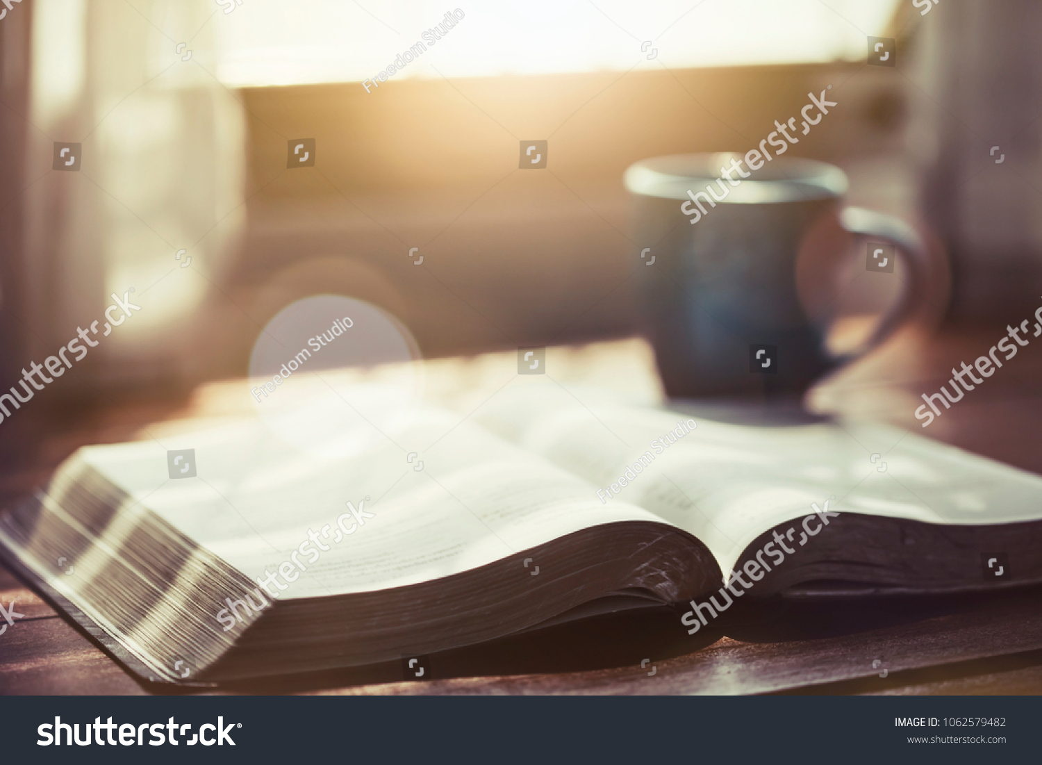 close up of open bible with a cup of coffee for morning devotion on wooden table with window light #1062579482