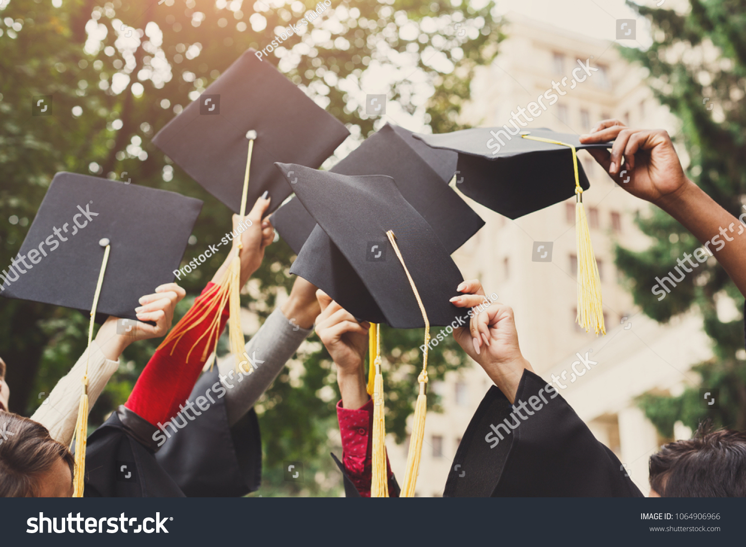 A group of multietnic students celebrating their graduation by throwing caps in the air closeup. Education, qualification and gown concept. #1064906966