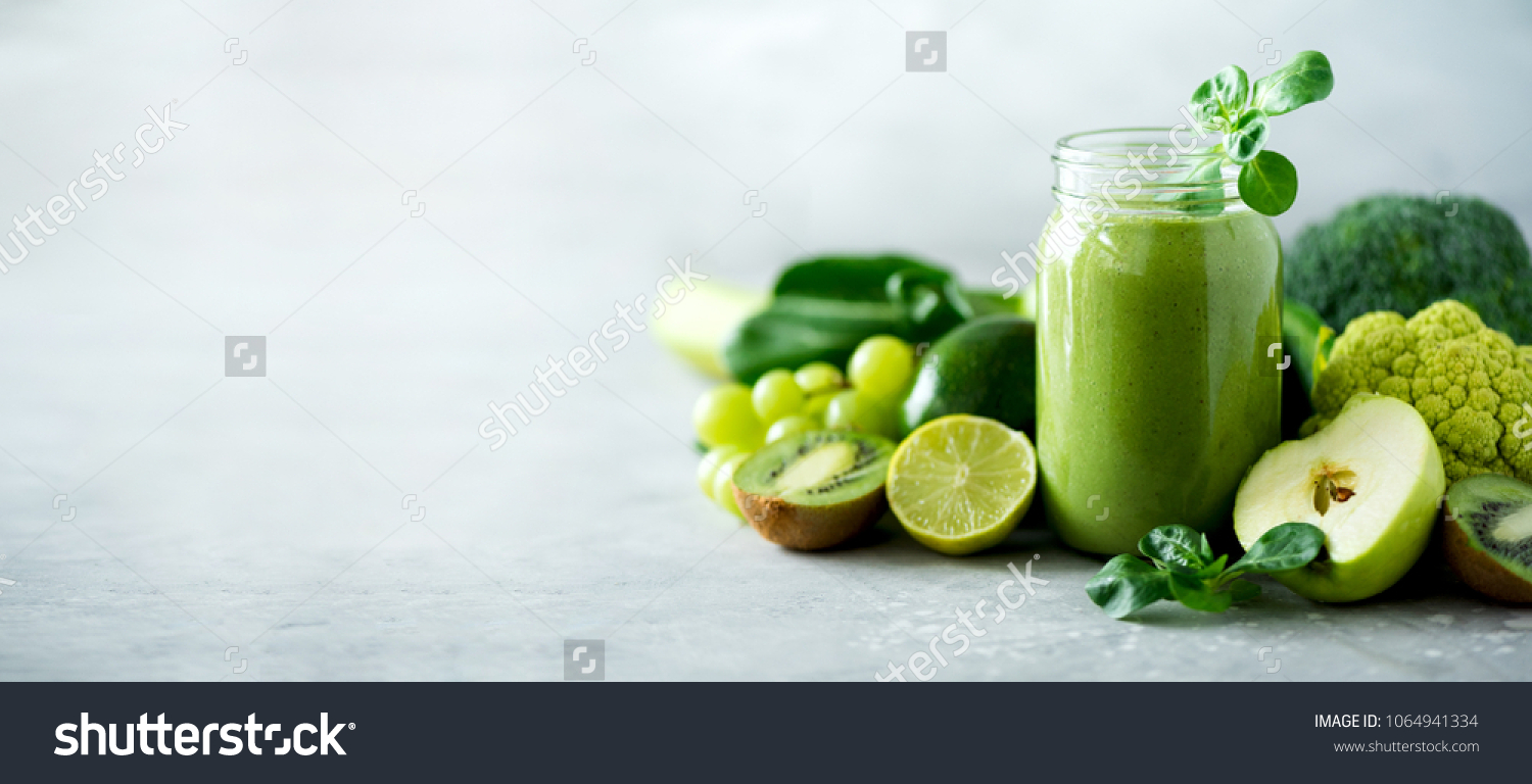 Glass jar mugs with green health smoothie, kale leaves, lime, apple, kiwi, grapes, banana, avocado, lettuce. Copy space. Raw, vegan, vegetarian, alkaline food concept. Banner. #1064941334