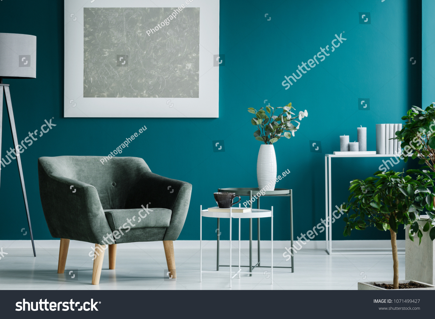 Green armchair against blue wall with silver painting in living room interior with plants #1071499427
