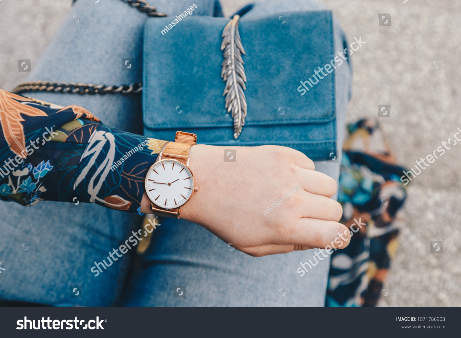 street style fashion details. close up, young fashion blogger wearing a floral jacker, and a white and golden analog wrist watch. checking the time, holding a beautiful suede leather purse.
 #1071786908