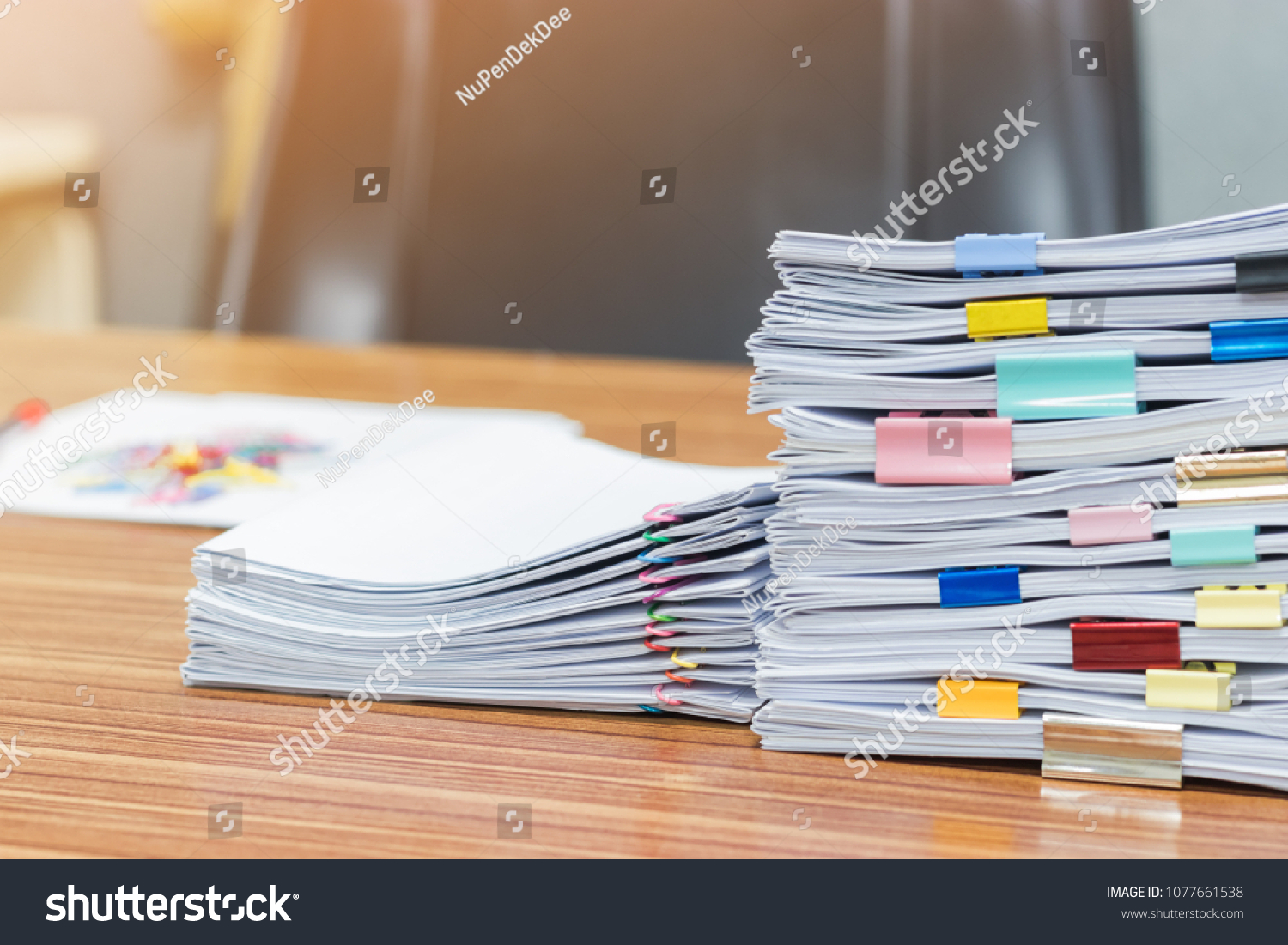 Stack of student's homework that assigned to students to be completed outside class on teacher's desk separated by colored paper clips. Document stacks arranged by various colored paper clips on desk. #1077661538