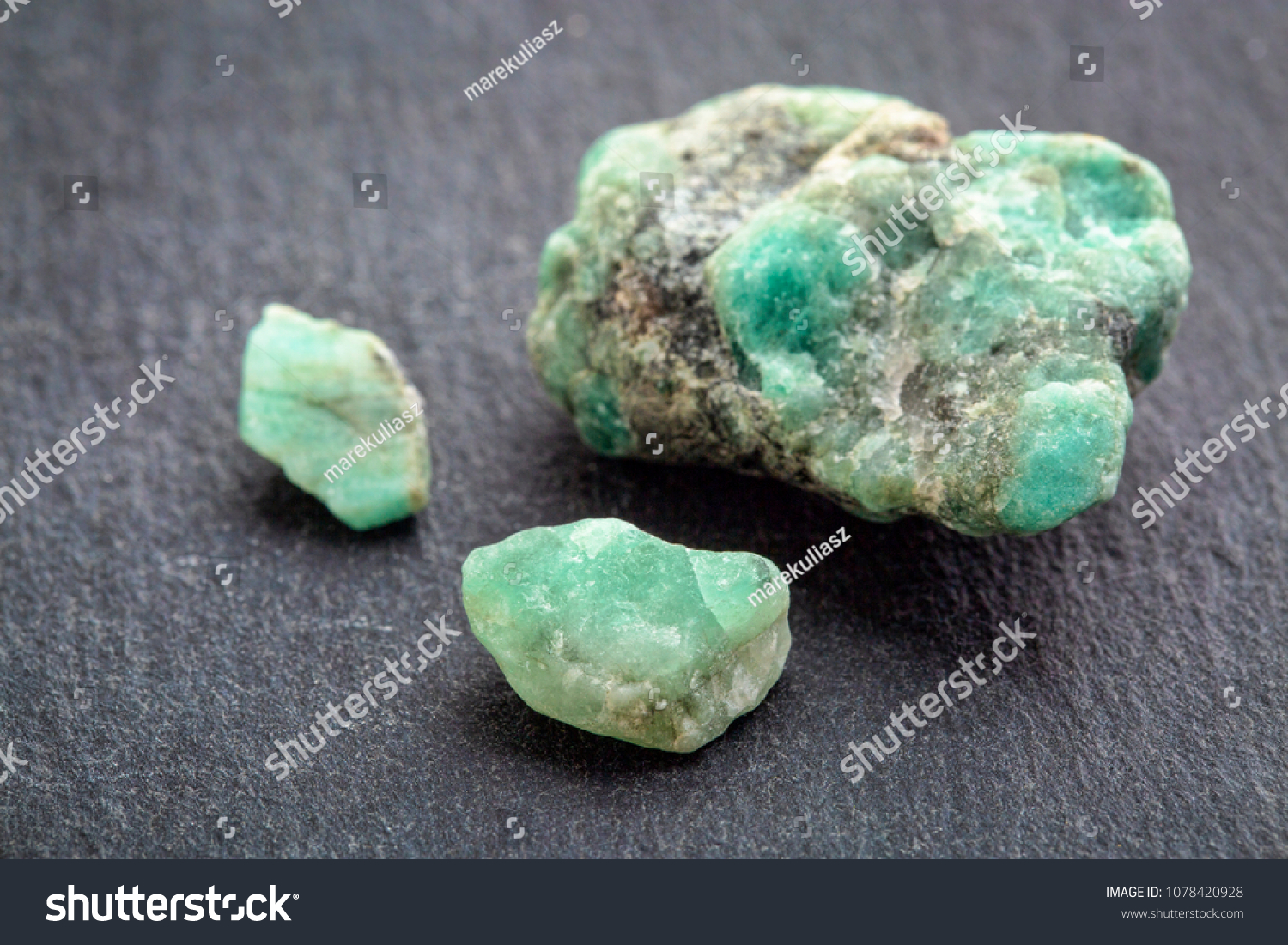 raw emerald gemstones (mineral beryl) with inclusions mined in Brazil on a gray slate stone #1078420928