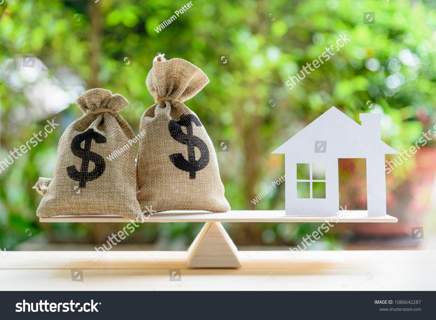 Home loan / reverse mortgage or transforming assets into cash concept : House paper model , US dollar hessian bags on a wood balance scale, depicts a homeowner or a borrower turns properties into cash #1086642287