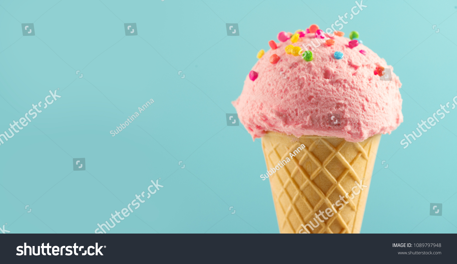 Ice cream cone close-up. Pink Icecream scoop in waffle cone over blue background. Strawberry or raspberry flavor Sweet dessert decorated with colorful sprinkles, closeup #1089797948