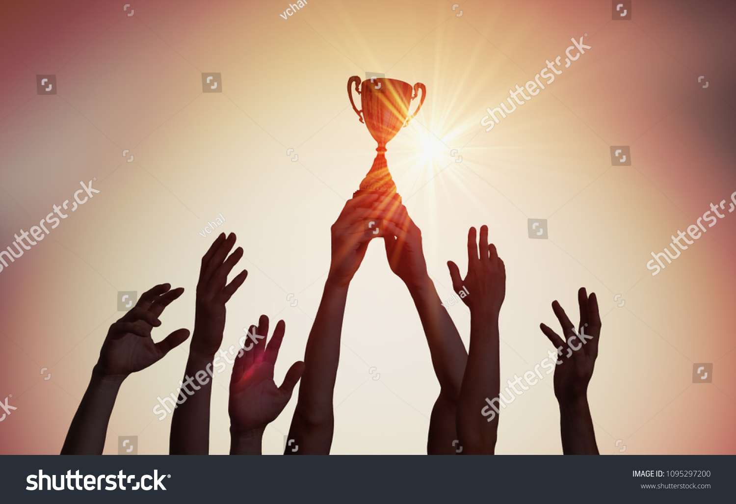 Winning team is holding trophy in hands. Silhouettes of many hands in sunset. #1095297200