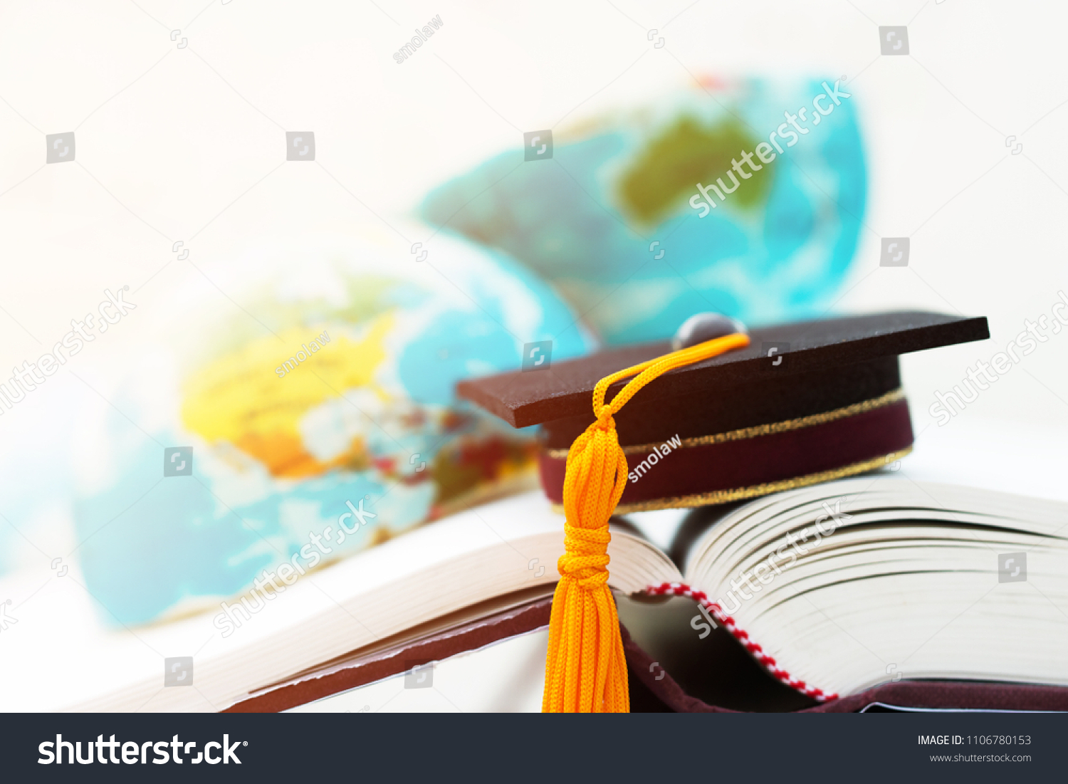 Graduate or Education knowledge learning study abroad concept : Graduation cap on opening textbook with blur of america australia earth world globe model map in Library room of campus, Back to School  #1106780153