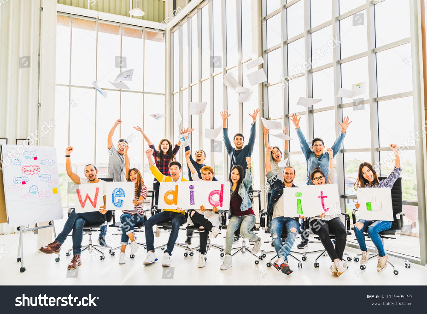 Multiethnic diverse group of happy business people cheering together, celebrate project success with papers wrote words We did it. Coworkers teamwork, career job achievement, or small business concept #1119809195