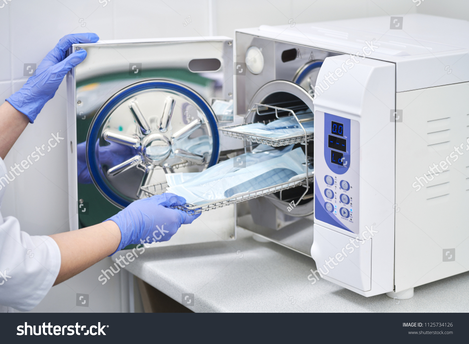 Sterilizing medical instruments in autoclave. Dental office. Dentist assistant's hands get out sterilizing medical instruments from autoclave. Selective focus. Sterile dental tools
 #1125734126