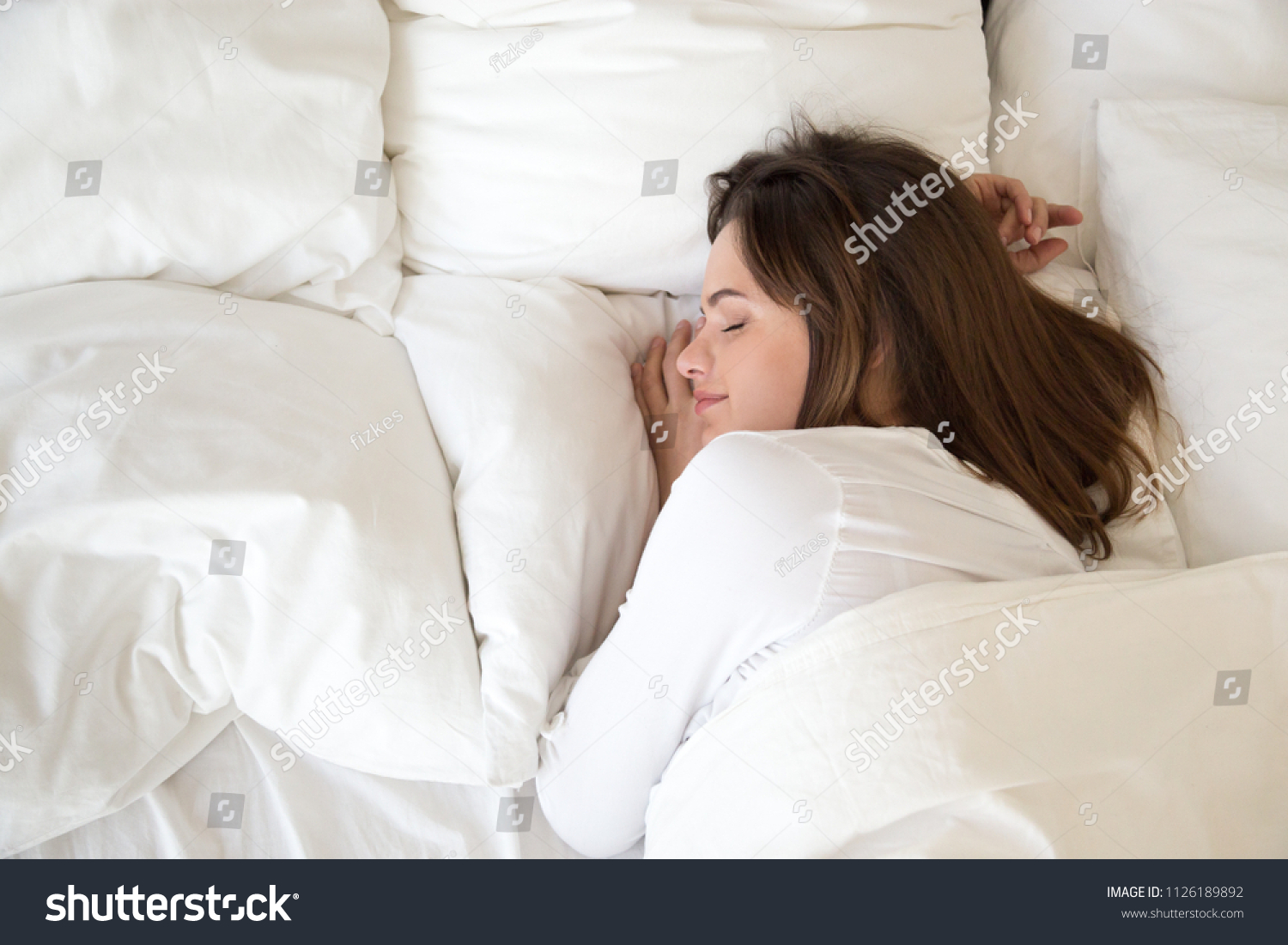 Millennial woman sleeping well on soft pillow and comfortable bed mattress with white cotton sheets under warm duvet having good night sleep enjoying sweet dreams and enough rest concept, top view #1126189892