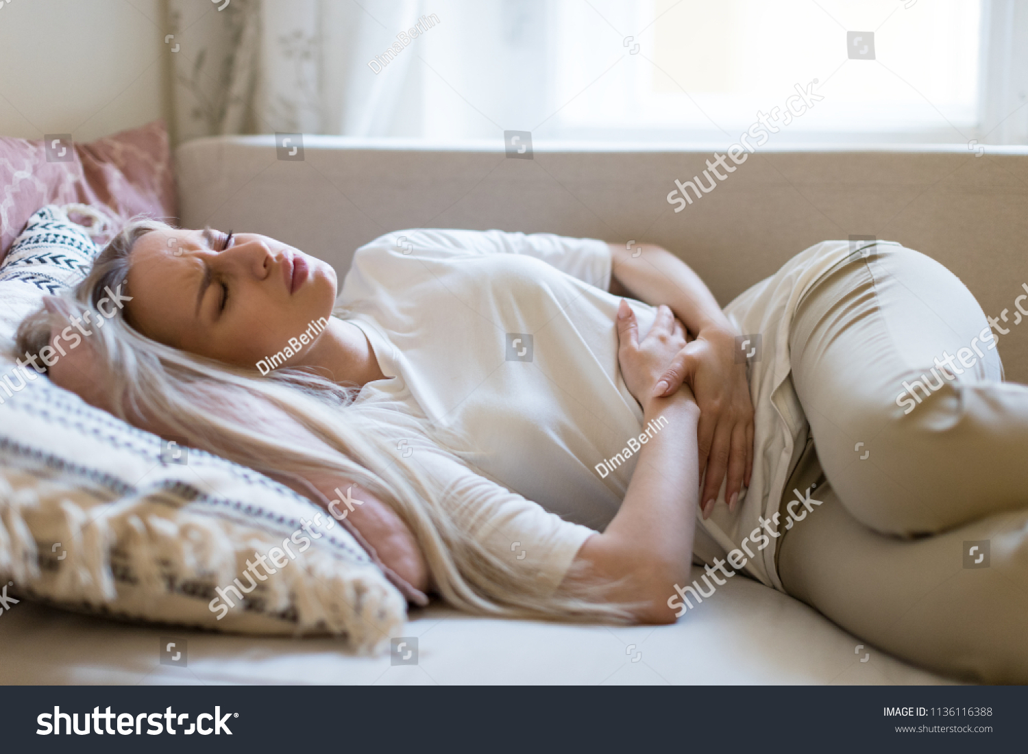 Health issues problems.Young Caucasian woman suffering from stomach pain, feeling abdominal pain or cramps, lying on sofa.Period menstruation, female health problem, aching belly and gynecology #1136116388