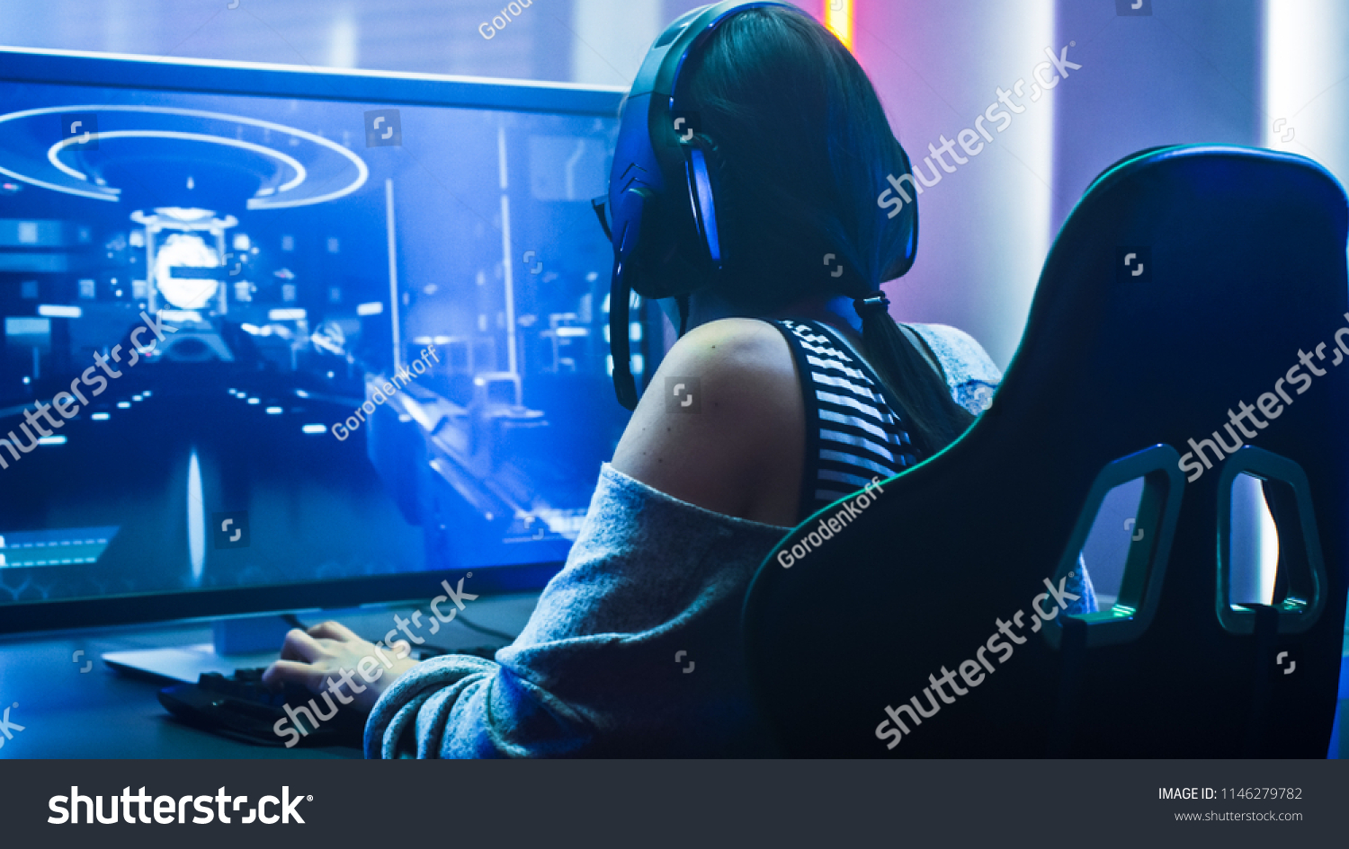 Shot of the Beautiful Pro Gamer Girl Playing in First-Person Shooter Online Video Game on Her Personal Computer. Casual Cute Geek wearing Glasses and Headset. Neon Room. eSport Cyber Games Internet #1146279782