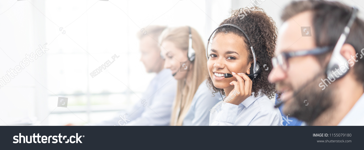 Call center worker accompanied by her team. Smiling customer support operator at work. Young employee working with a headset. #1155079180