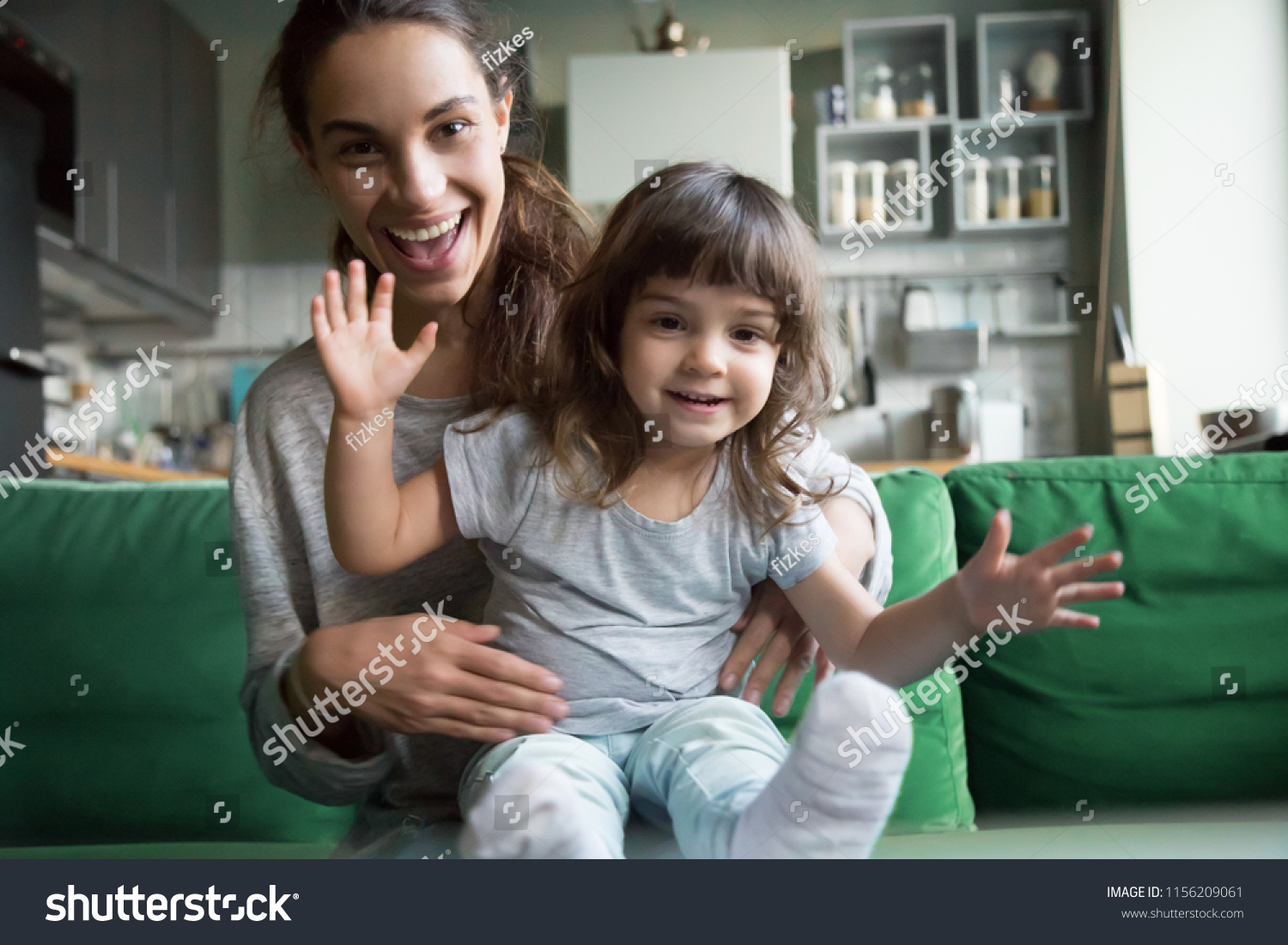Portrait of happy excited young mother and kid girl waving hands looking at camera, smiling mom with child daughter making video call, family vloggers recording video blog or vlog together concept #1156209061