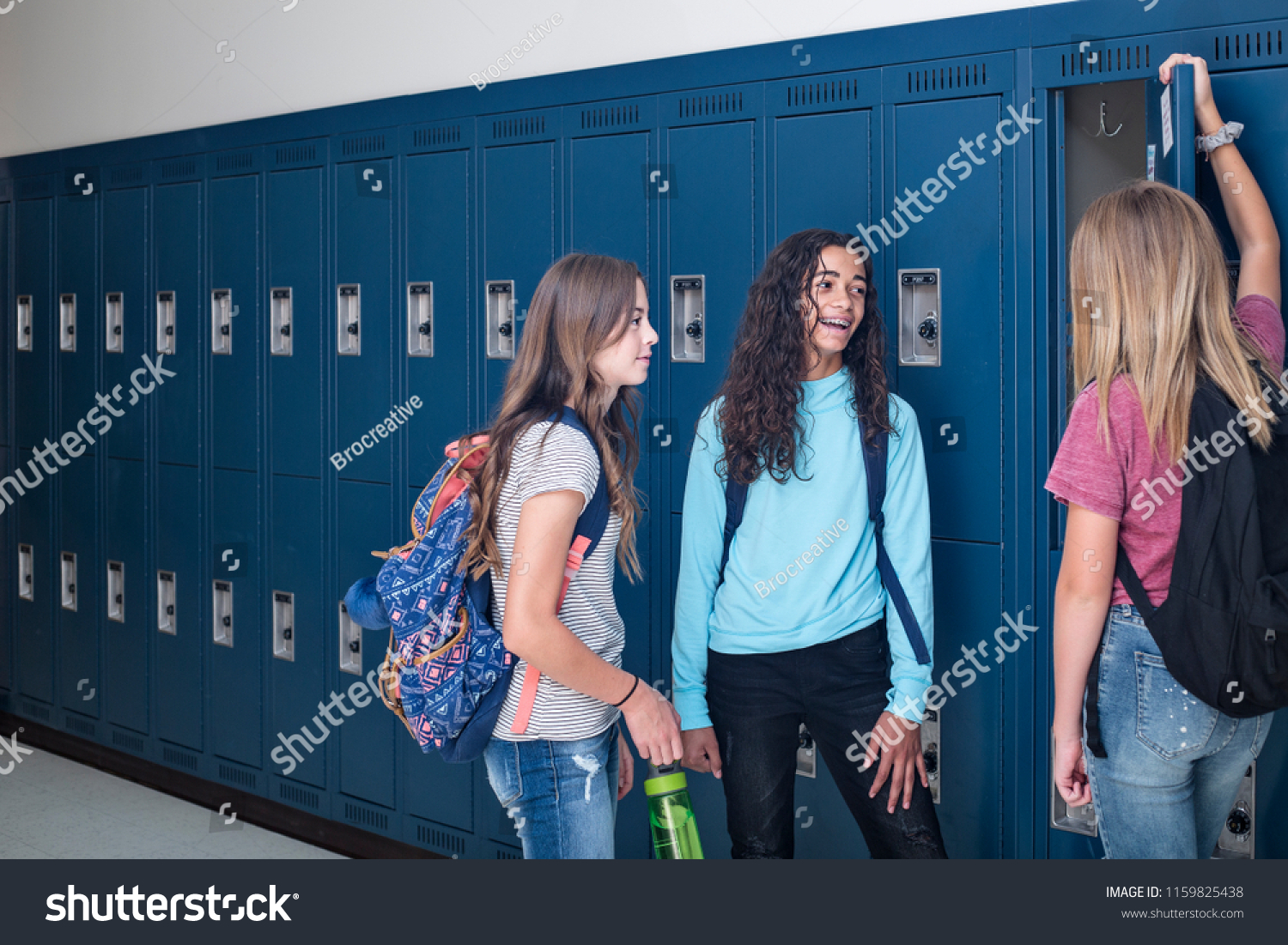 Candid photo of Three Junior High school Students talking together in a school hallway. Diverse Female school girls smiling and having fun together during a break at school standing by their lockers #1159825438
