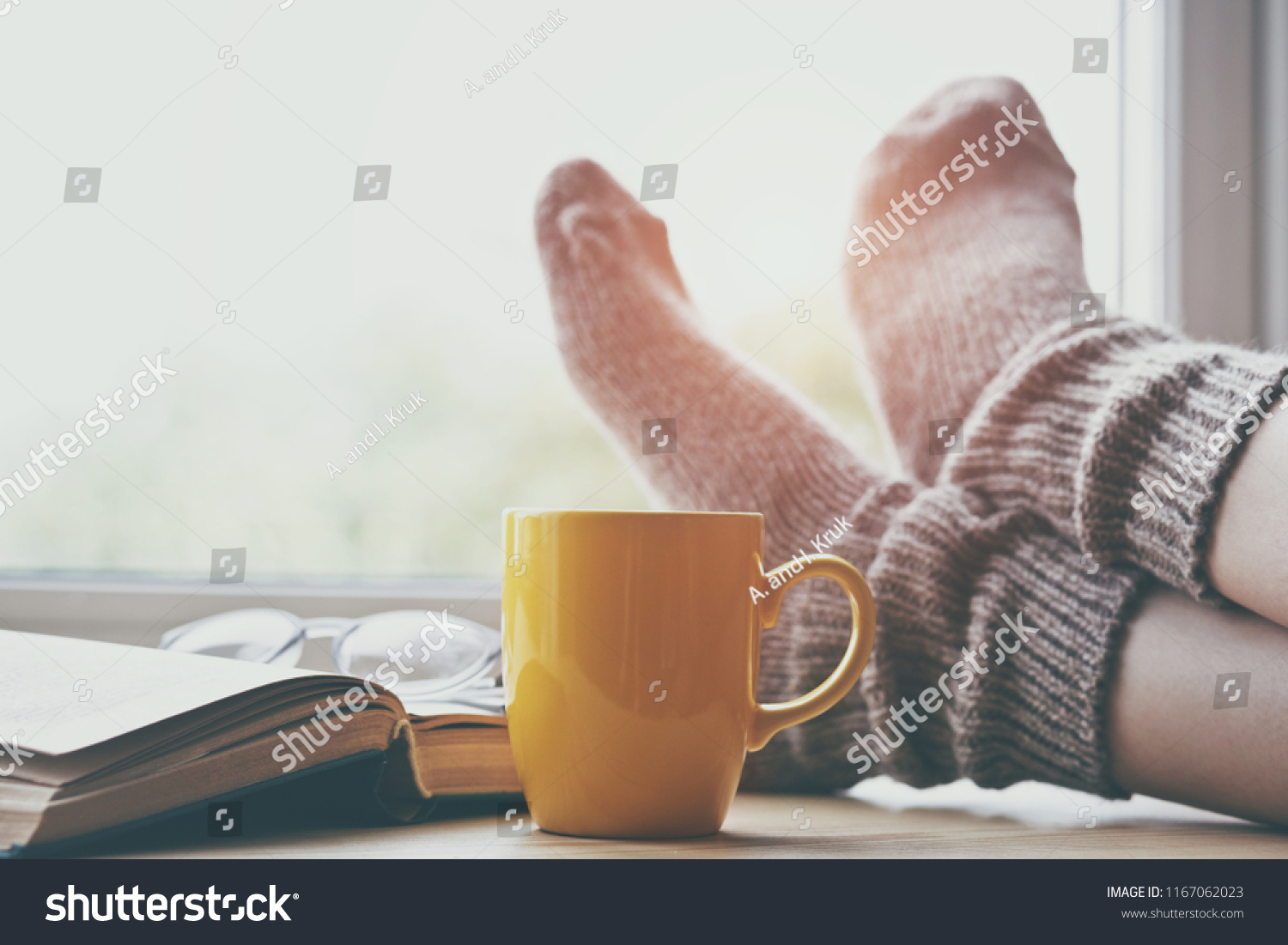Woman resting keeping legs in warm socks on table with morning coffee and reading book #1167062023