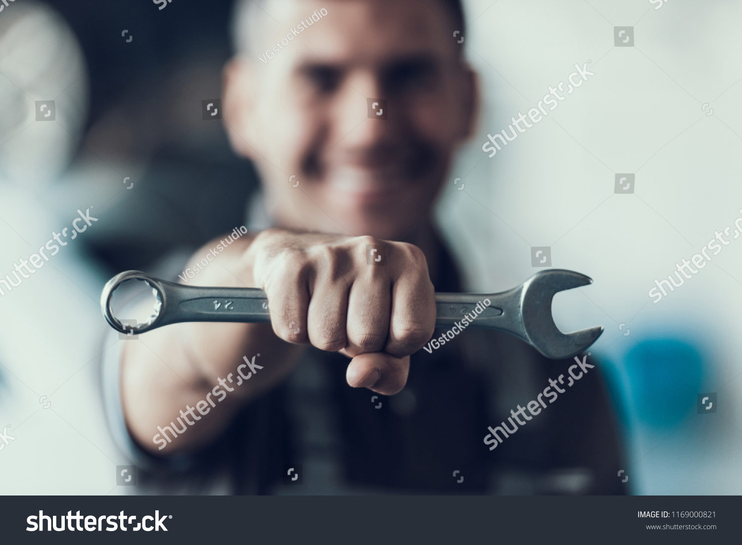 Auto Mechanic with Tool on Blurred Background. Close-up of Repairman Strong Fist Holding Metalic Wrench in Garage. Automobile Repair Service Concept. Automobile Master Concept #1169000821
