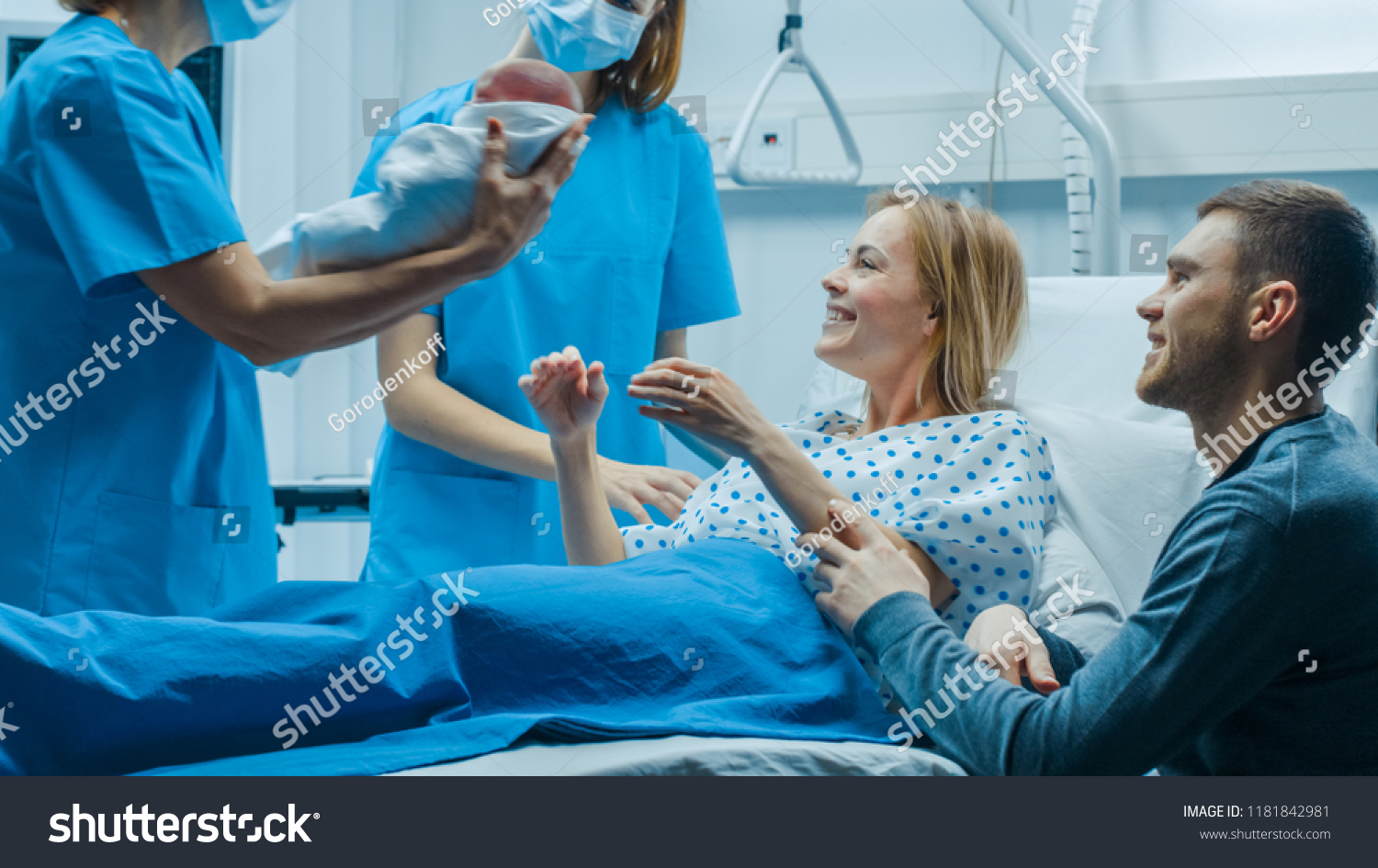 In the Hospital Midwife Gives Newborn Baby to a Mother to Hold, Supportive Father Sitting Near Wife. Happy Family in the Modern Delivery Ward. #1181842981