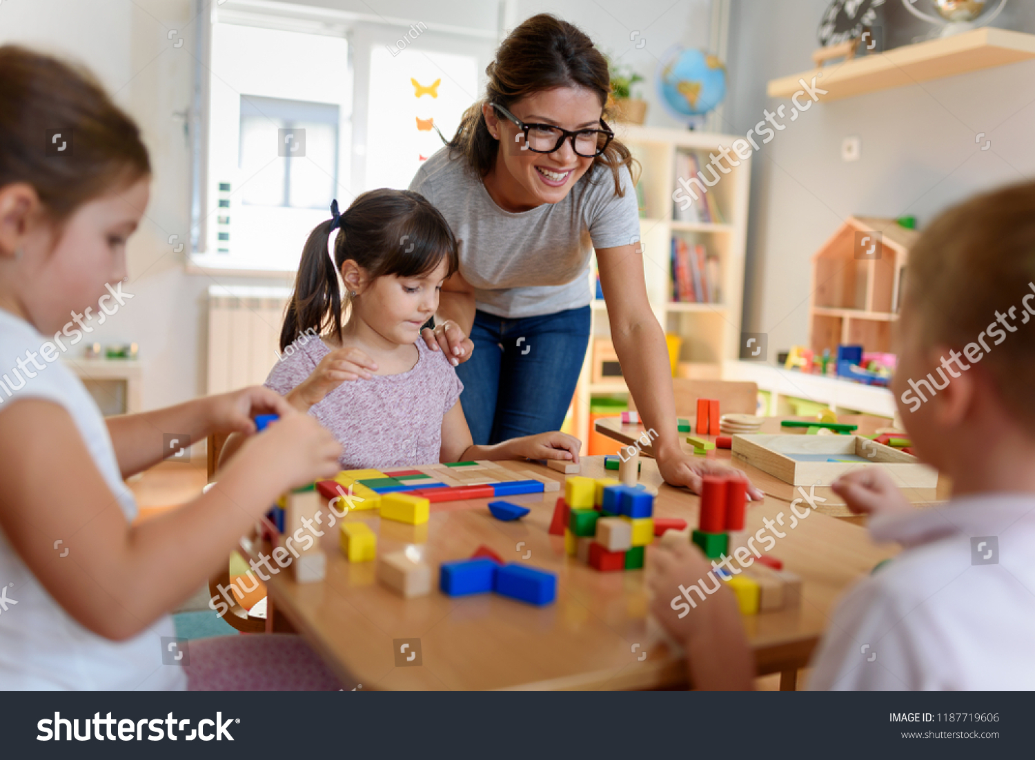 Preschool teacher with children playing with colorful wooden didactic toys at kindergarten #1187719606