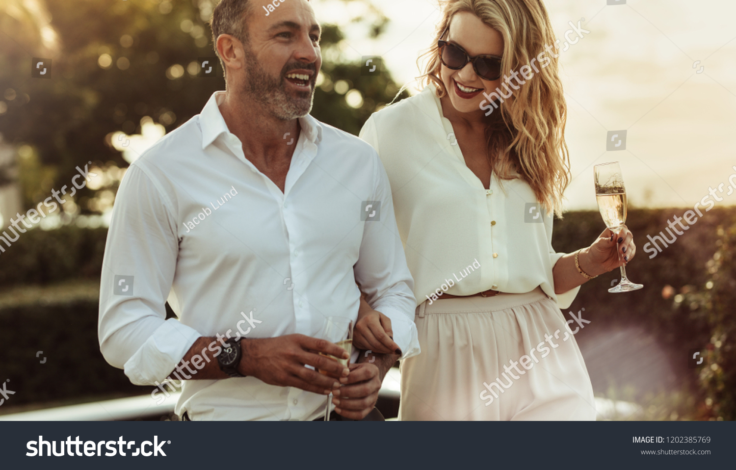 Cheerful man and woman with a drink outdoors. Wealthy couple together with a glass of wine. #1202385769