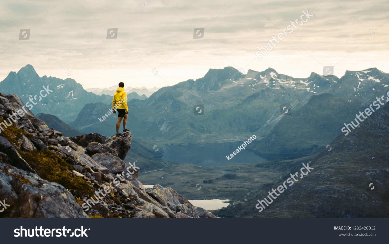 
Adventurous man is standing on top of the mountain and enjoying the beautiful view during a vibrant sunset. Beautiful Nature Norway natural landscape aerial photography #1202420002