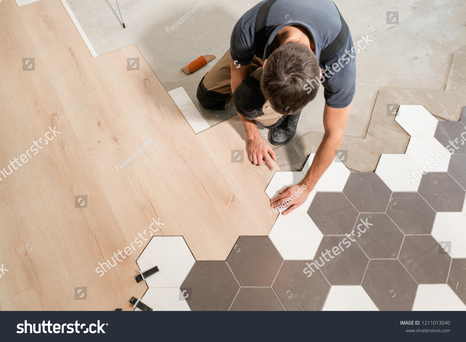 Male worker installing new wooden laminate flooring. The combination of wood panels of laminate and ceramic tiles in the form of honeycomb. Kitchen renovation. #1211013040
