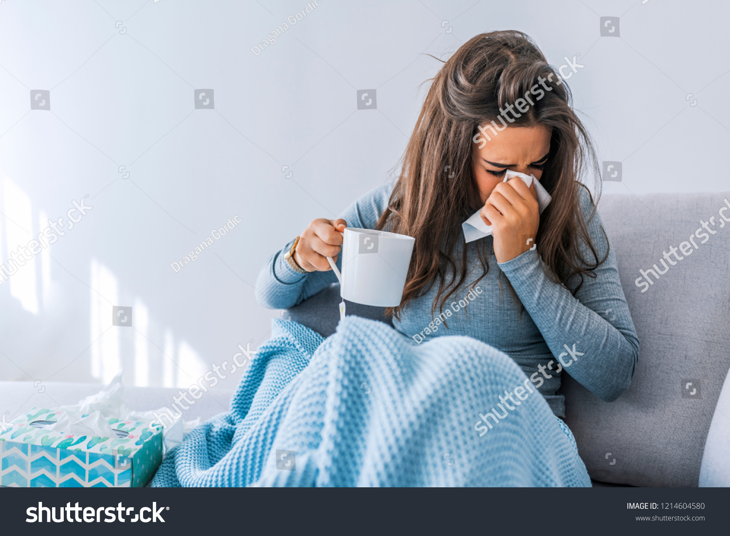 Sick woman with headache sitting under the blanket. Sick woman with seasonal infections, flu, allergy lying in bed. Sick woman covered with a blanket lying in bed with high fever and a flu, resting.  #1214604580