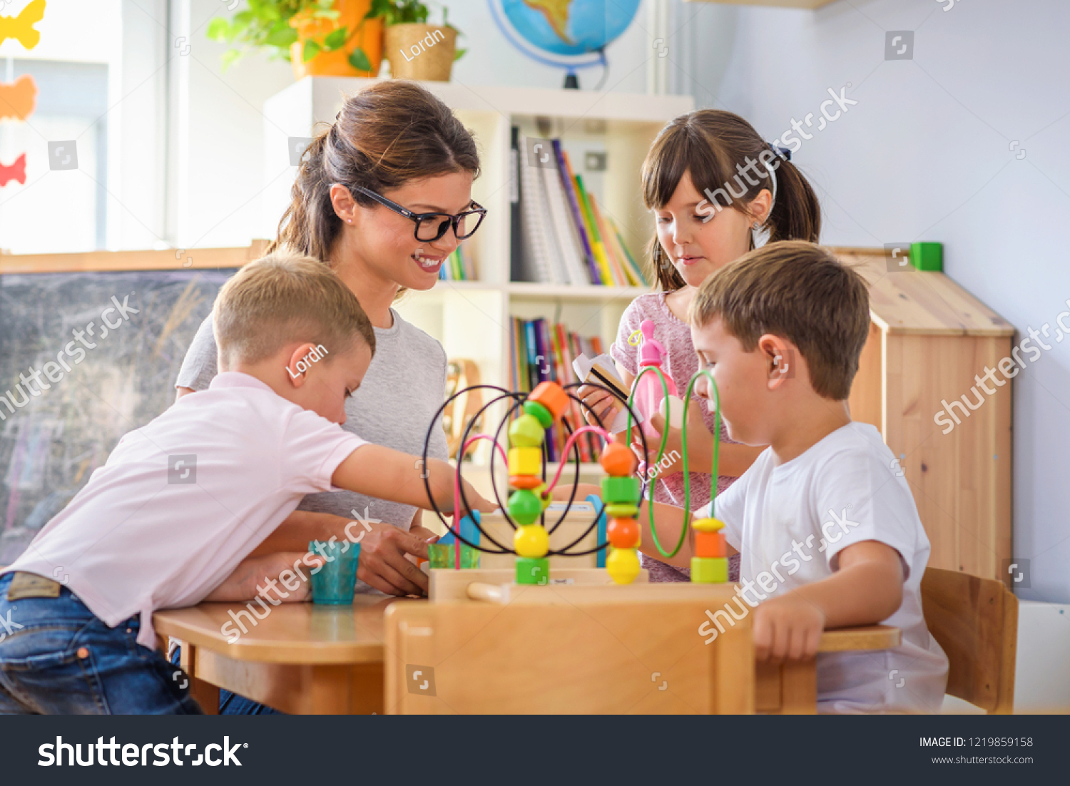 Preschool teacher with children playing with colorful wooden didactic toys at kindergarten #1219859158
