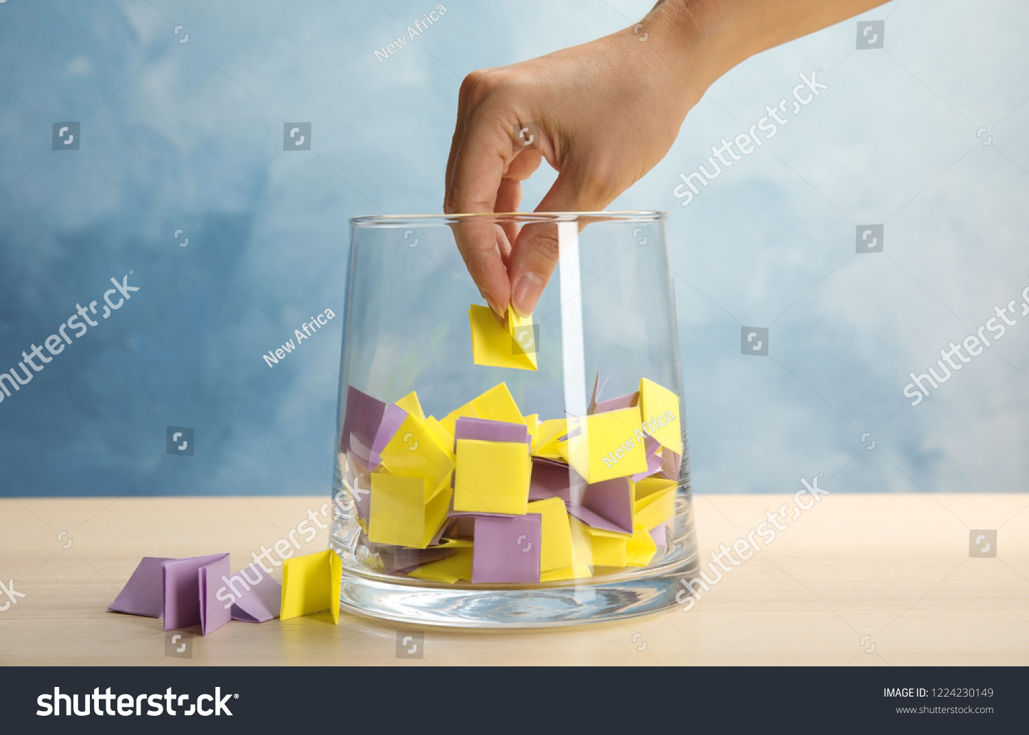 Woman taking paper piece from glass vase on table. Lottery #1224230149