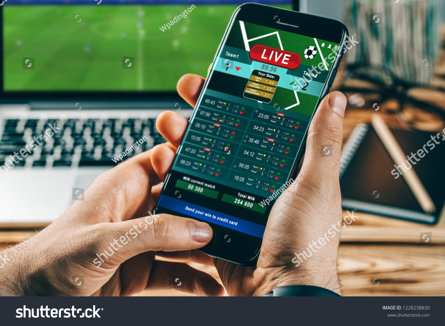 Close up cropped shot of male hands making bets using gambling mobile application on his phone. Man watching football match online broadcast on his laptop waiting for winning results.  #1228238830
