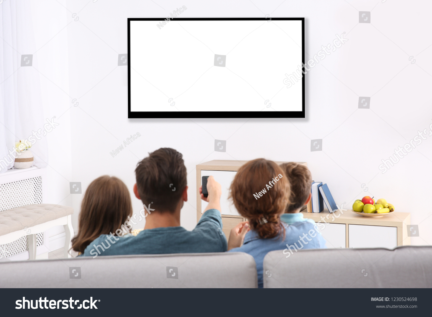 Family with remote control sitting on couch and watching TV at home, space for design on screen. Leisure and entertainment #1230524698