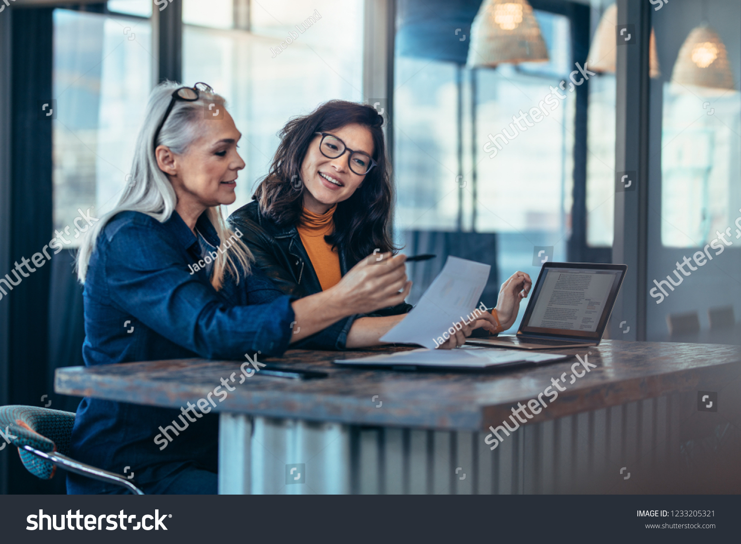Two women analyzing documents while sitting on a table in office. Woman executives at work in office discussing some paperwork. #1233205321