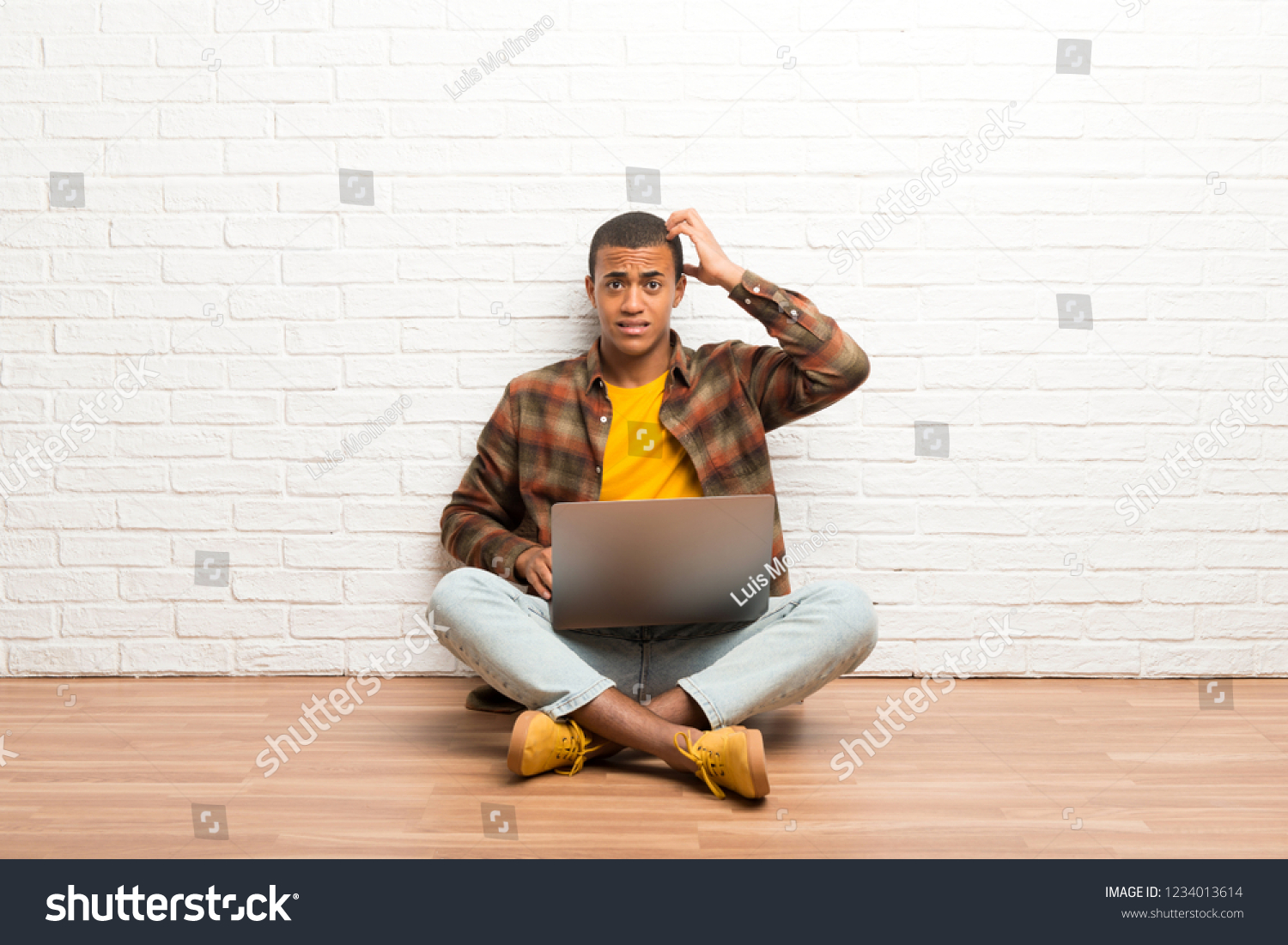 African american man sitting on the floor with his laptop with an expression of frustration and not understanding #1234013614