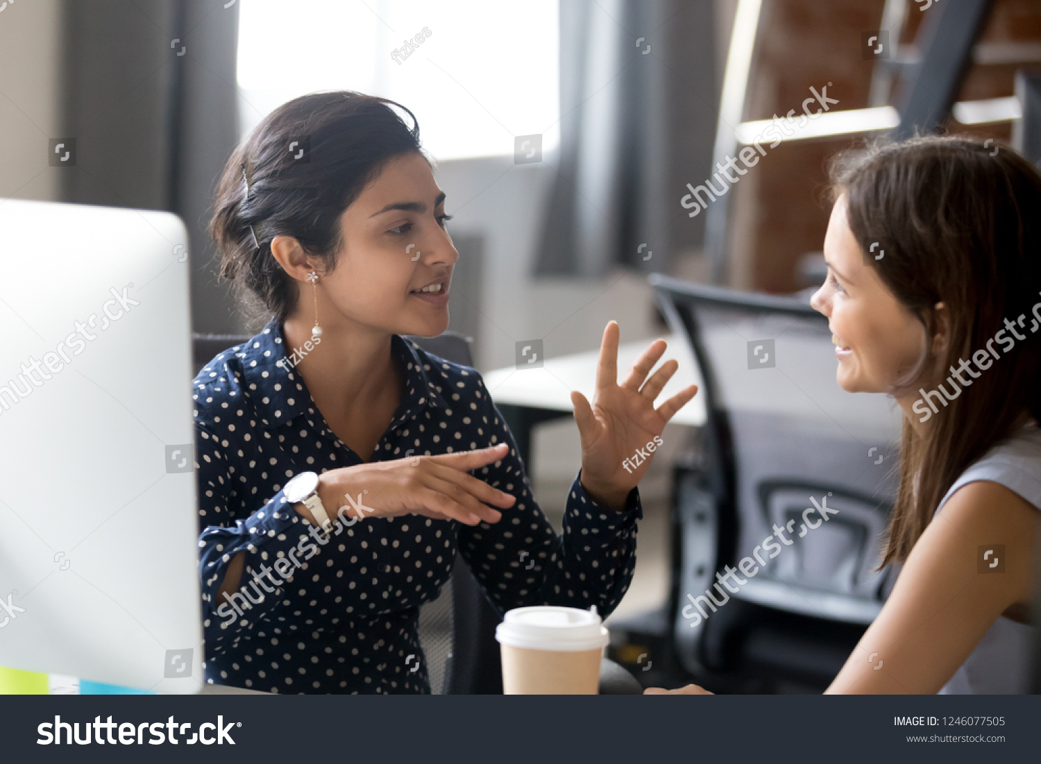 Friendly female colleagues having good relationships, pleasant conversation at workplace during coffee break, smiling young woman listen talkative coworker, discussing new project, talking in office #1246077505
