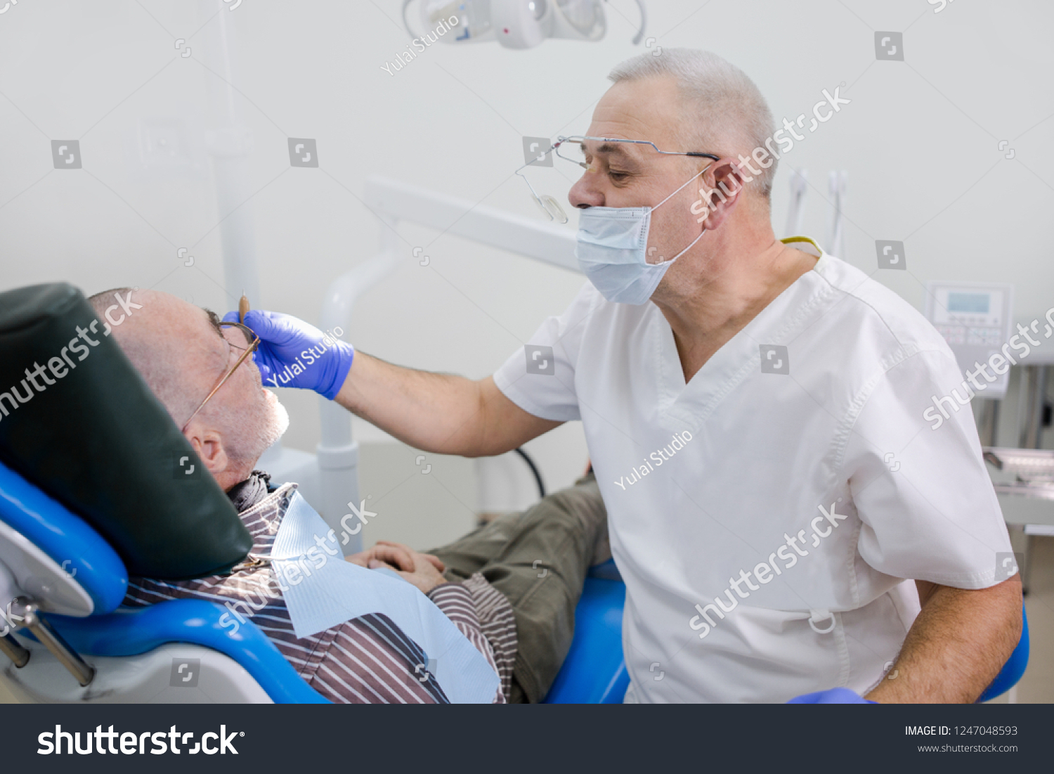 Adult dentist examines the oral cavity of his grandfather in a dental clinic #1247048593