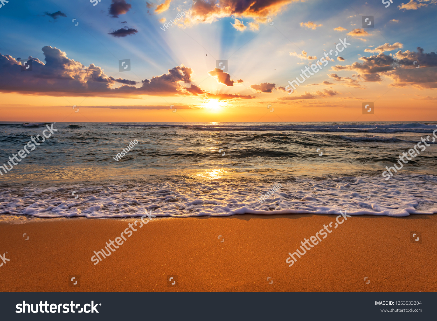 Colorful ocean beach sunrise with deep blue sky and sun rays. #1253533204