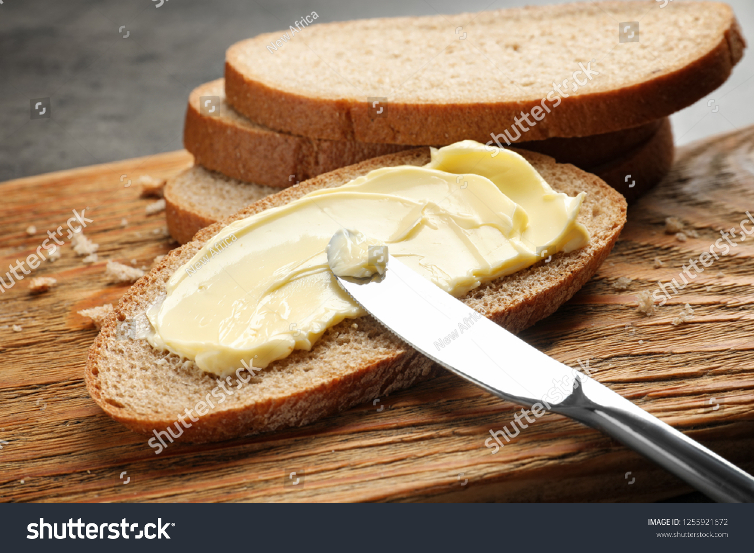Spreading butter onto toast with knife on wooden board #1255921672