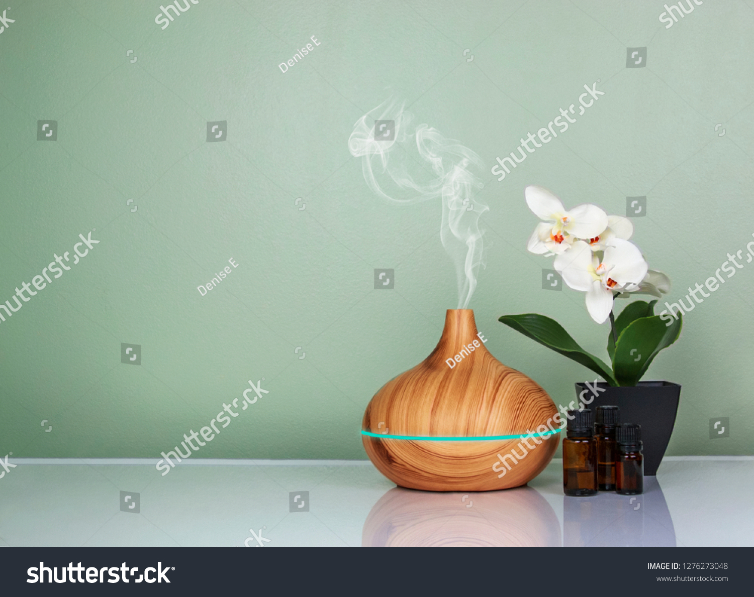 Electric Essential oils Aroma diffuser, oil bottles and flowers on light green surface with reflection. #1276273048